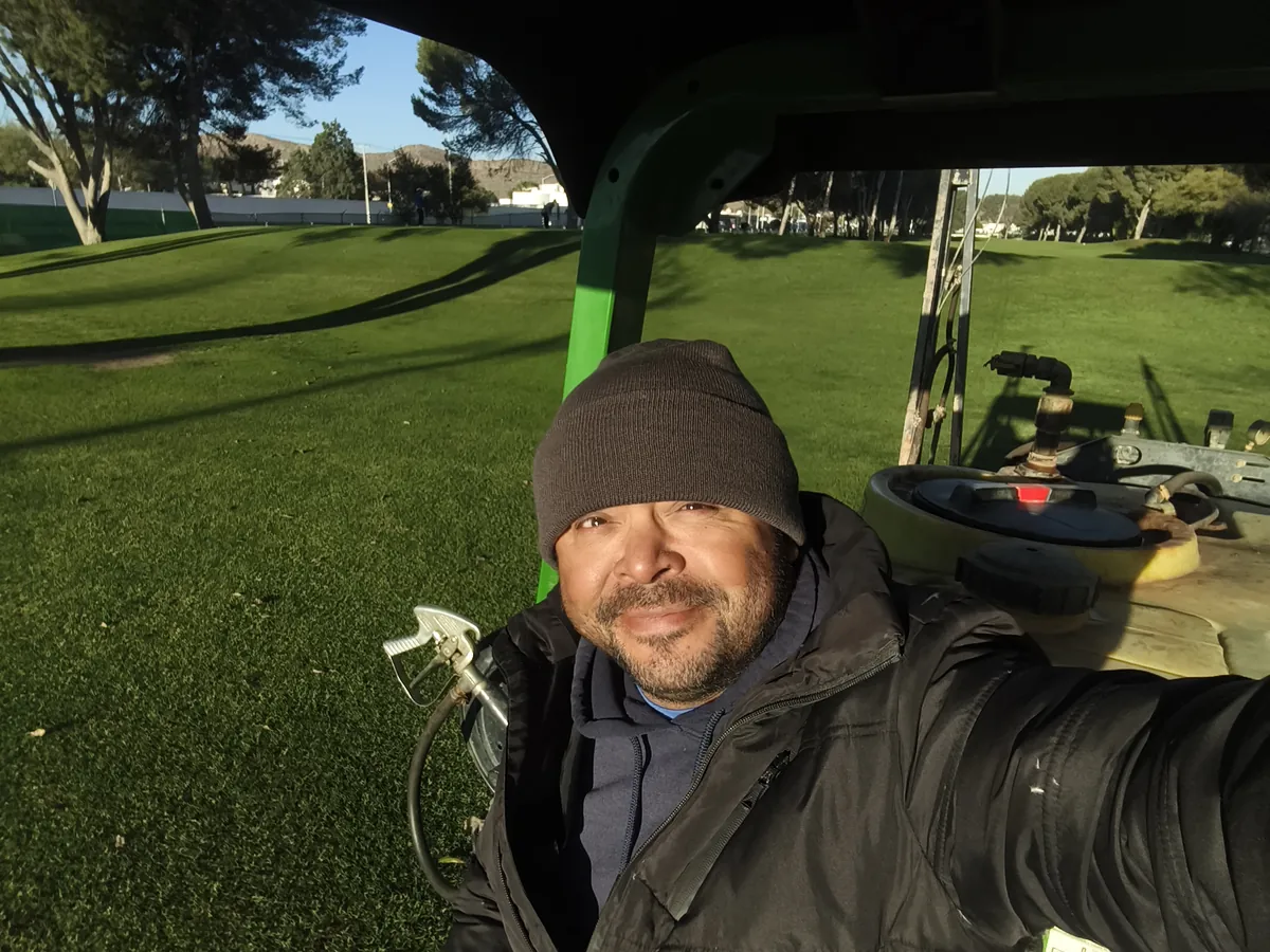 Ezekiel Robles in a beanie and work jacket, on a utility cart on a golf course